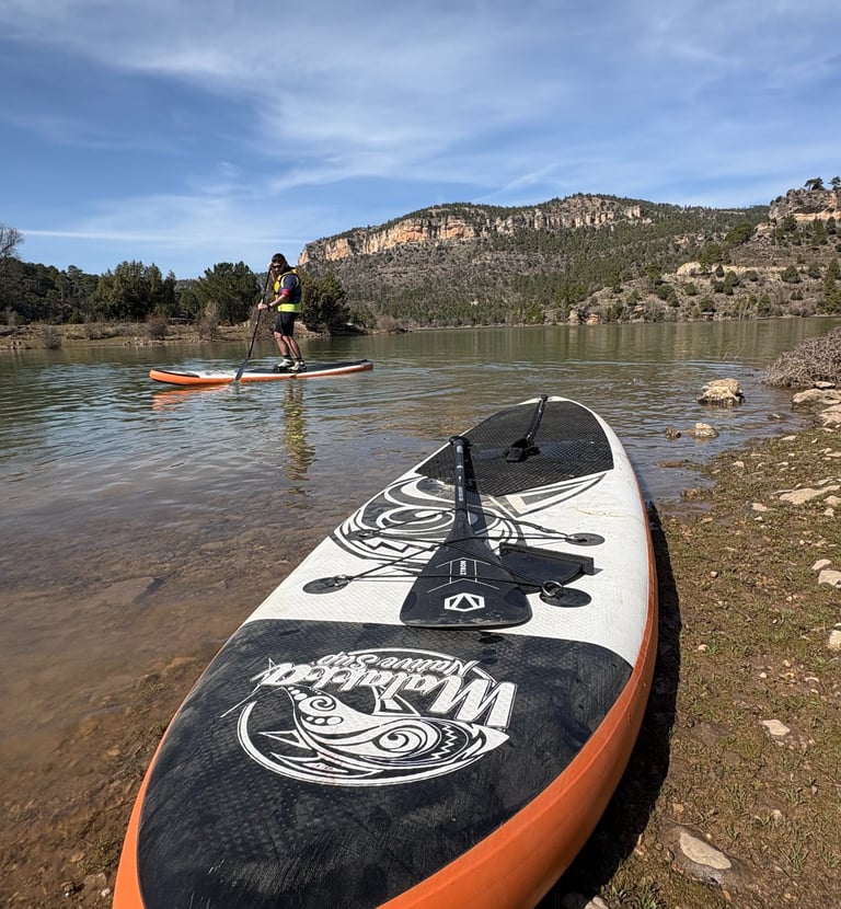 Paddle Surf en la orilla del embalse de la Toba con grandes montañas al fondo y una persona haciendo