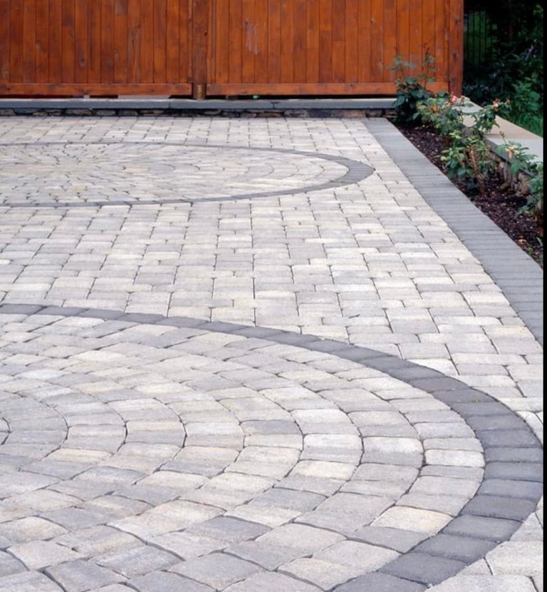 Backyard patio featuring circular stone paver designs and a dark grey border next to a wooden fence.