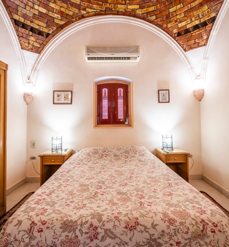 Rustic bedroom with floral bedding, wooden wardrobe, and unique vaulted brick ceiling design.