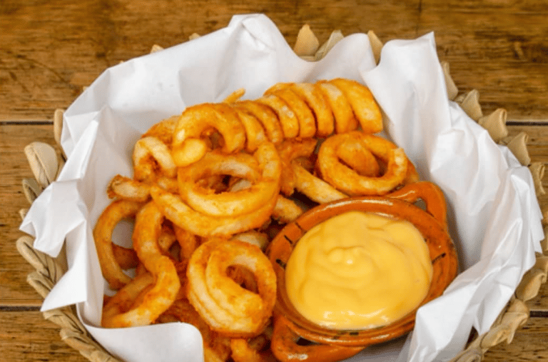 Papas fritas en espiral, crujientes y sazonadas, servidas en una cesta con una salsa cremosa.