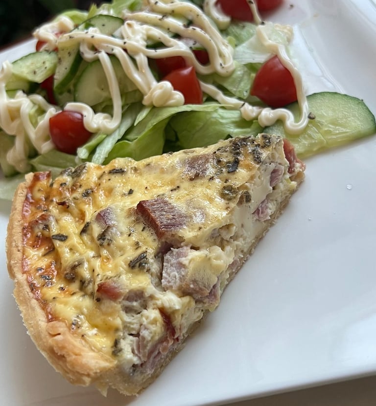 A slice of homemade quiche lorraine served with a fresh garden salad on a white plate.