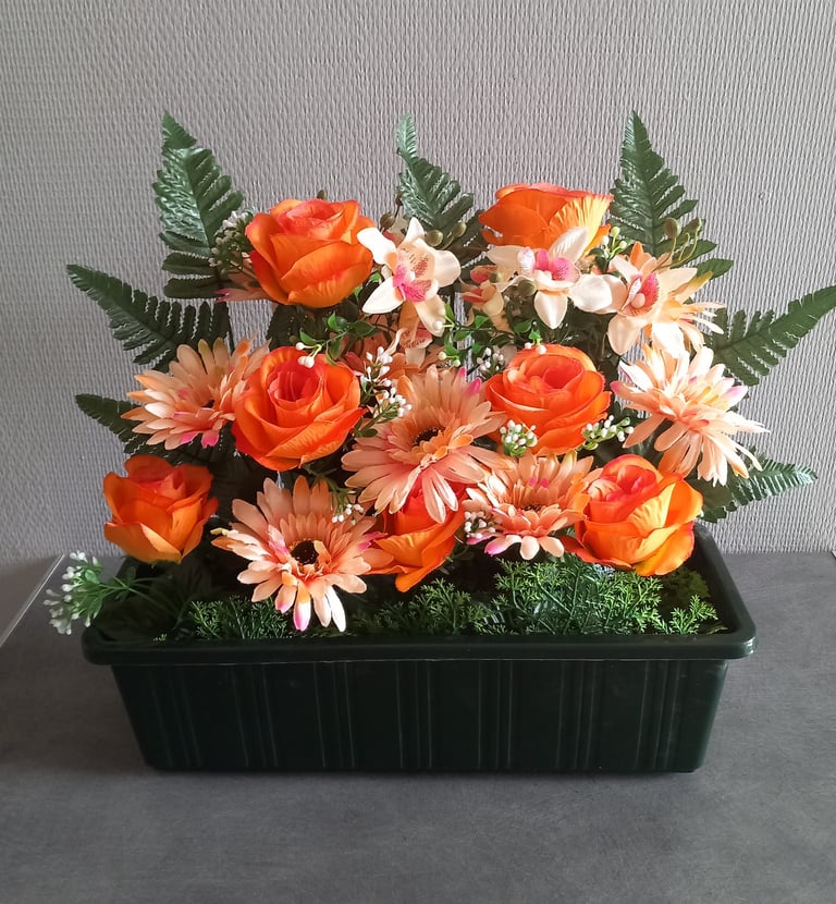 Roses orange artificielles et marguerites de gerbera pêche dans une jardinière décorative noire avec