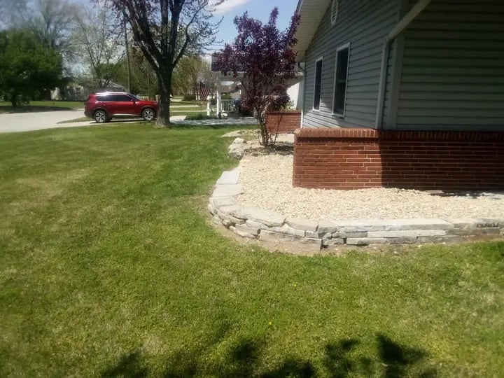 Residential landscaping featuring a low natural stone retaining wall and decorative gravel bed.
