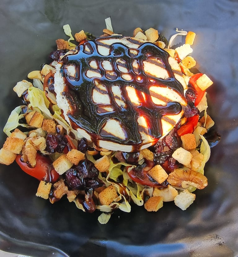 Warm goat cheese salad with balsamic glaze, crunchy croutons, and walnuts in a black bowl.