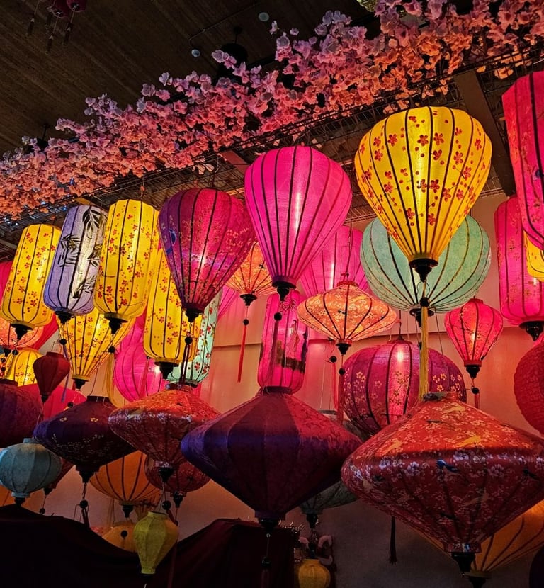 Vibrant colorful Vietnamese silk lanterns hanging under pink cherry blossoms at a cultural festival.