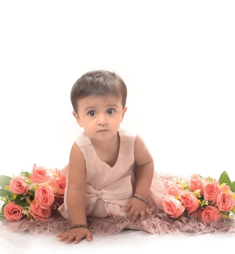 Baby girl in a pink dress sitting on a fuzzy rug surrounded by pink roses. Milestone Photography