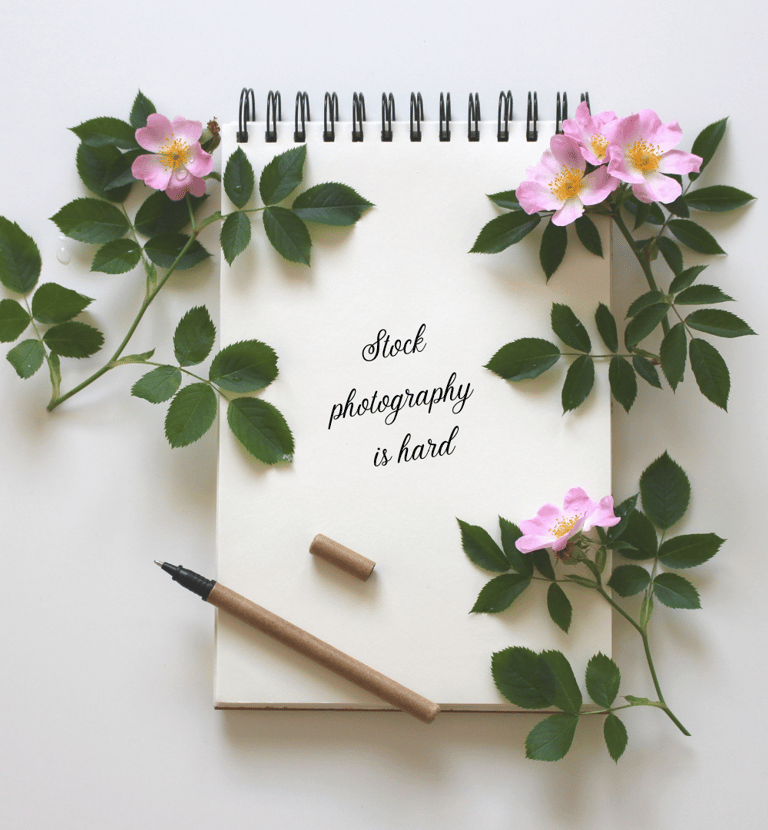 Spiral-bound notebook with pink dogwood flowers scattered about. "Stock photography is hard," written in black on the page.