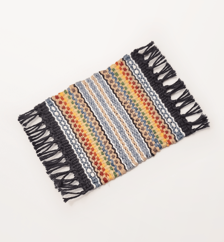 a hand-woven mug rug coaster with muted pride rainbow colours