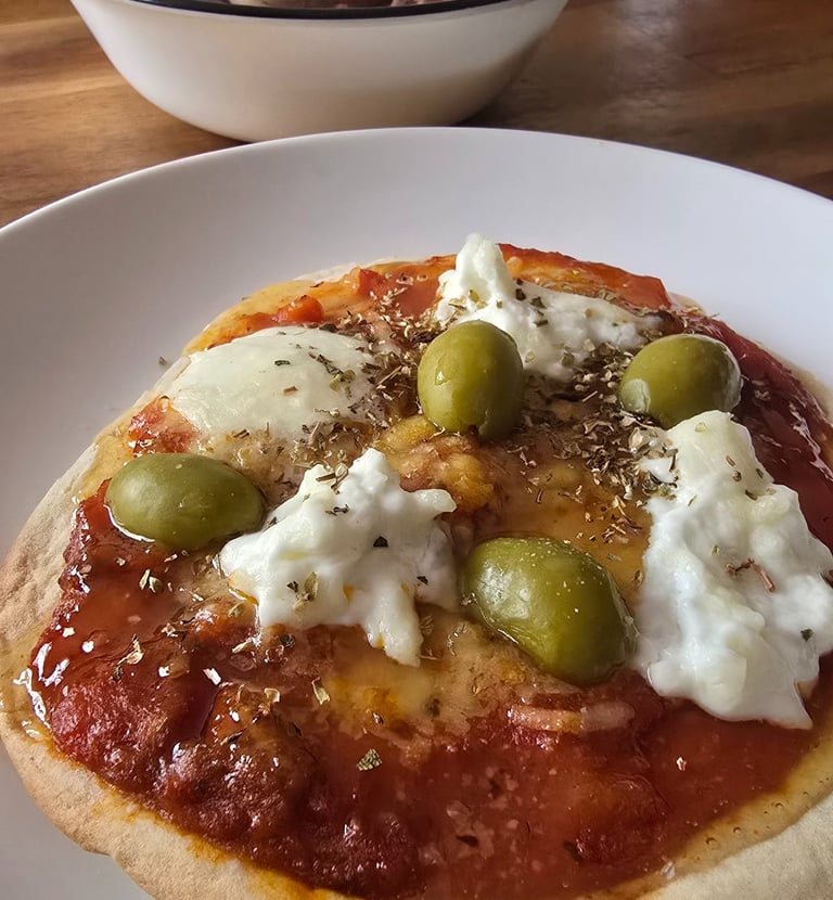 Pan pita con pasta de tomate y encima queso burrata y olivas verdes y oregano encima delciosos