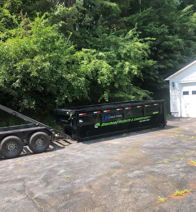 Black Load Trail roll-off dumpster on a driveway for residential waste management and landscaping.