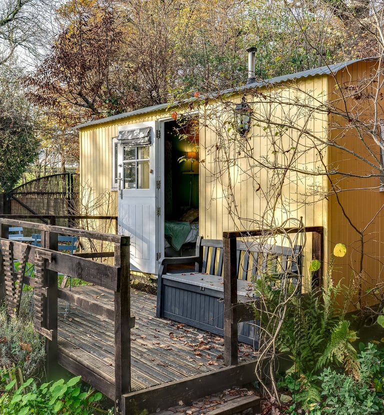 Yellow shepherd's hut with a wooden deck and 'LOVE' sign nestled in a lush garden.