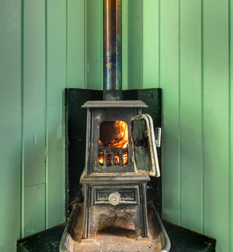 A small cast iron wood burning stove with an open door and glowing fire inside against green paneled walls.