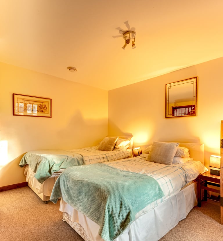 Cozy rustic bedroom with two twin beds, teal blankets, and wooden furniture under warm lighting.