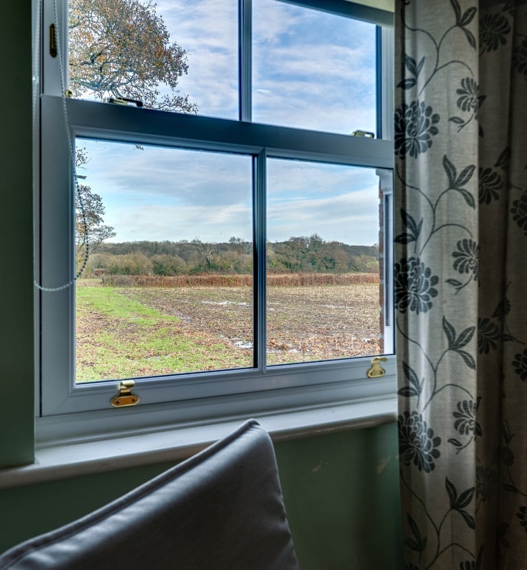 A white sash window with a view of a countryside landscape, rolling fields, and autumn trees.