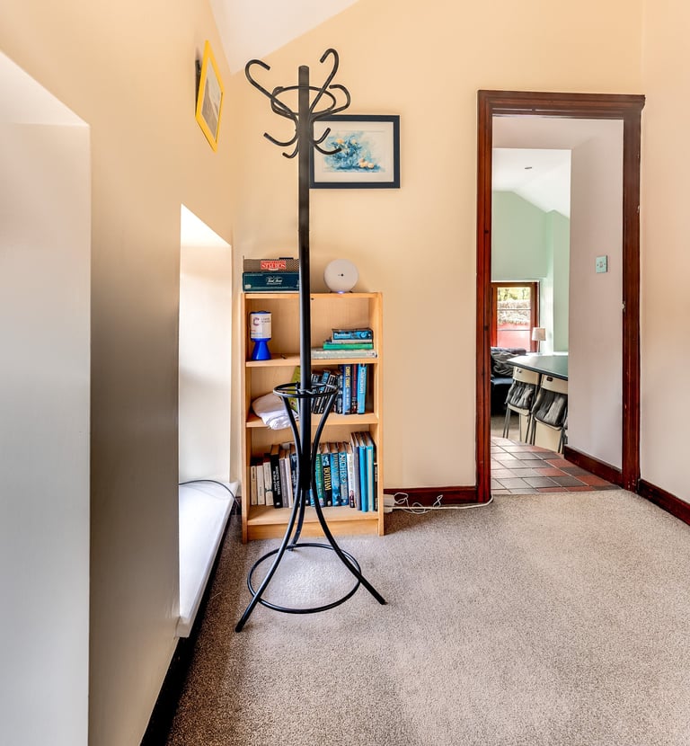 A carpeted hallway featuring a black metal coat rack and a wooden bookshelf with books.