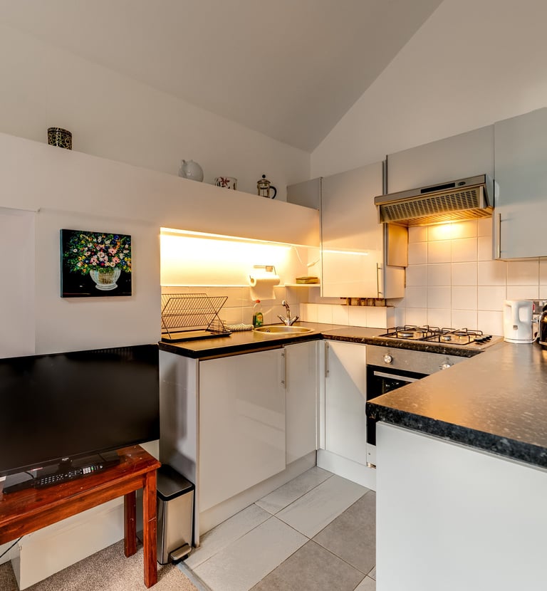 Modern small apartment kitchen with white cabinets, dark countertops, and integrated appliances.