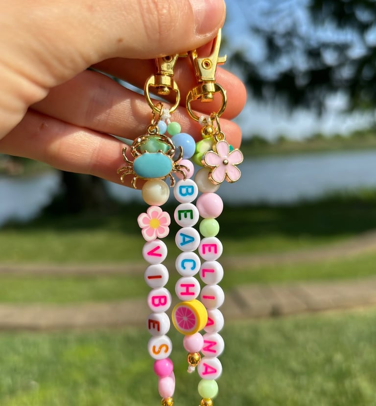 Mano sosteniendo dos llaveros, conformado por cuentas de letras, una flor y un cangrejo