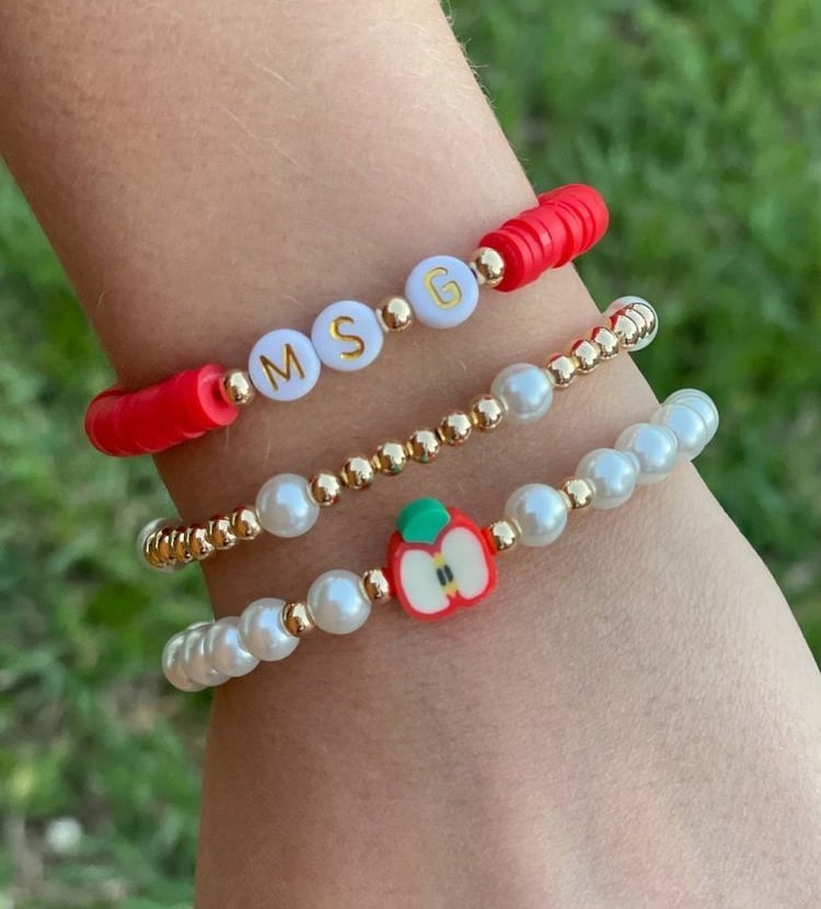 Mano con 3 pulseras diferentes, cuentas rojas, perlas, letras y un charm de manzana