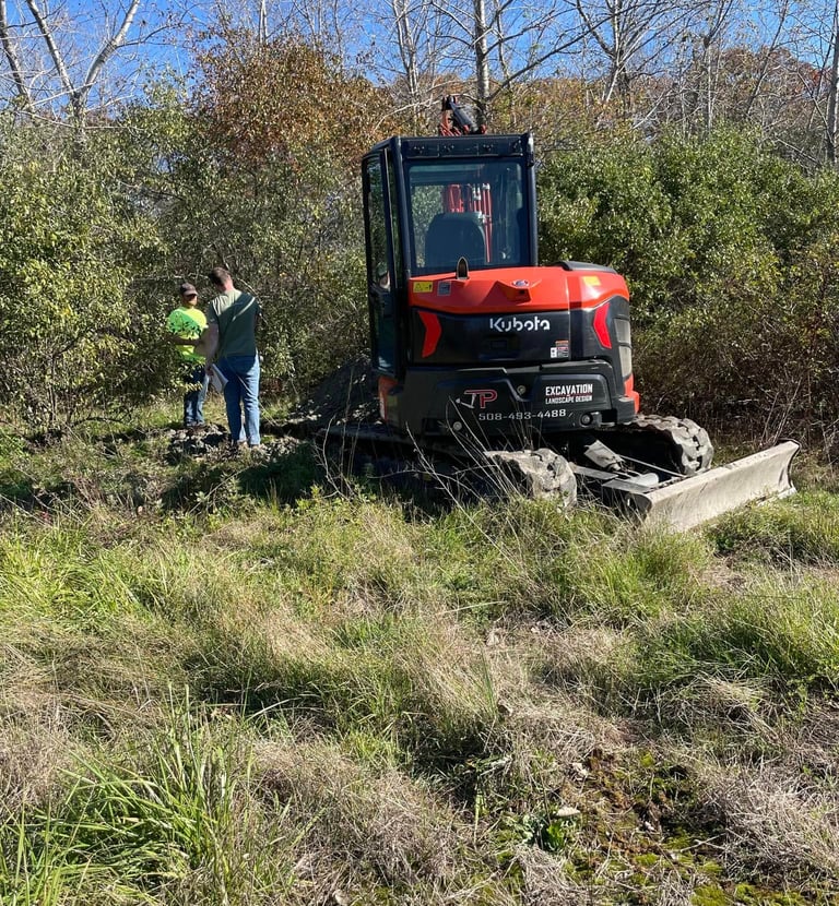 A Kubota mini excavator being used by JP Excavation for land clearing near a wooded area.