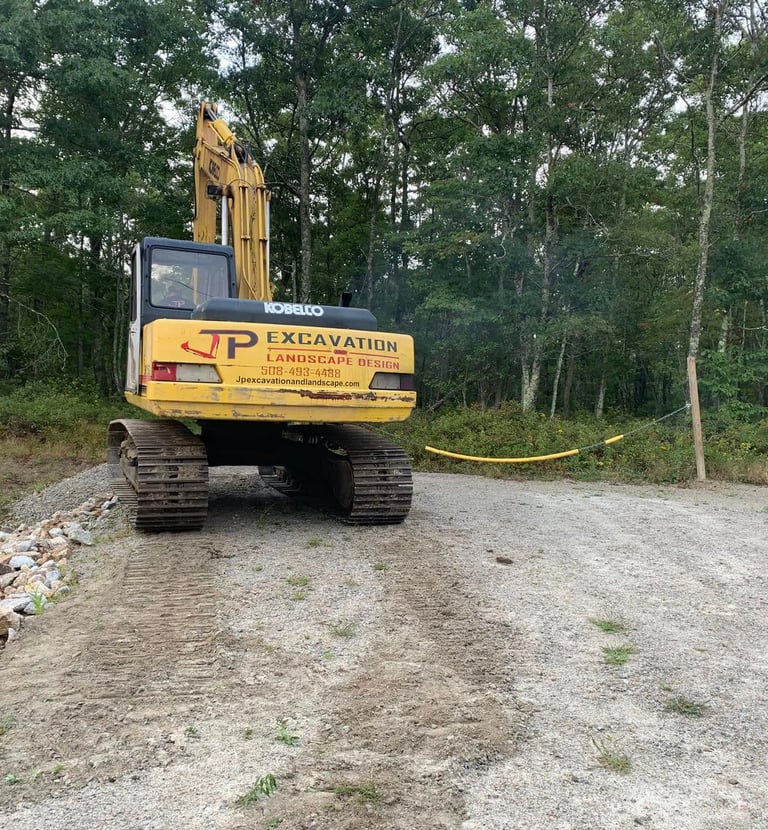 A yellow Kobelco excavator performing excavation and landscape design at a wooded construction site.