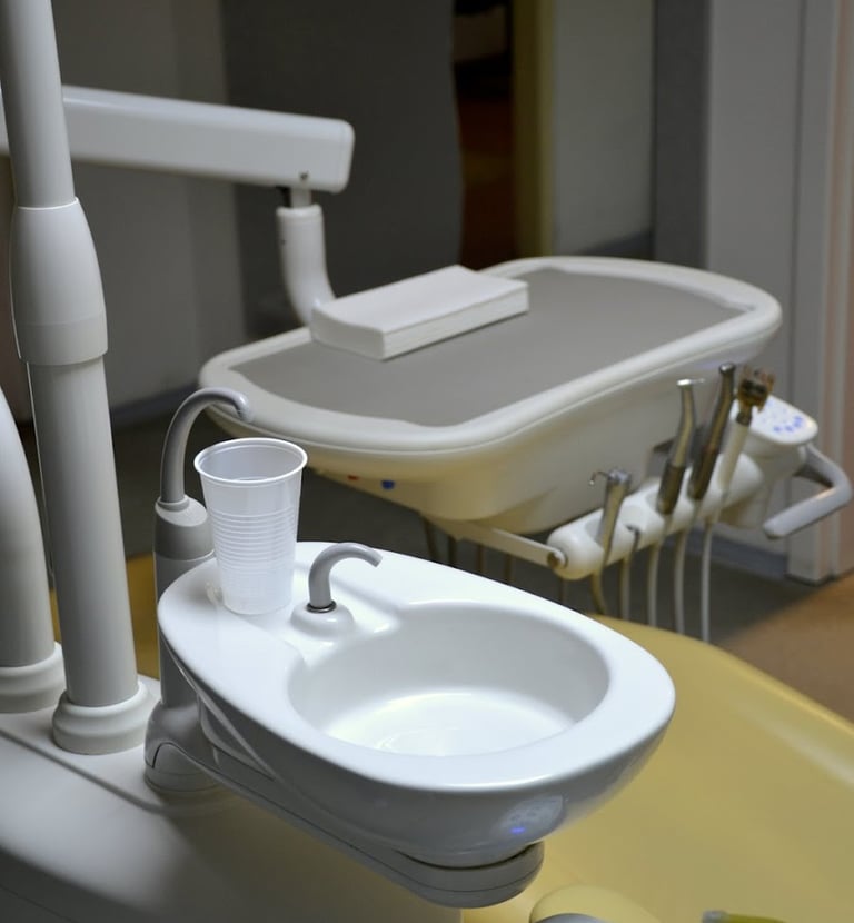 A dental examination unit with a ceramic spittoon, plastic rinse cup, and clinical tool tray.