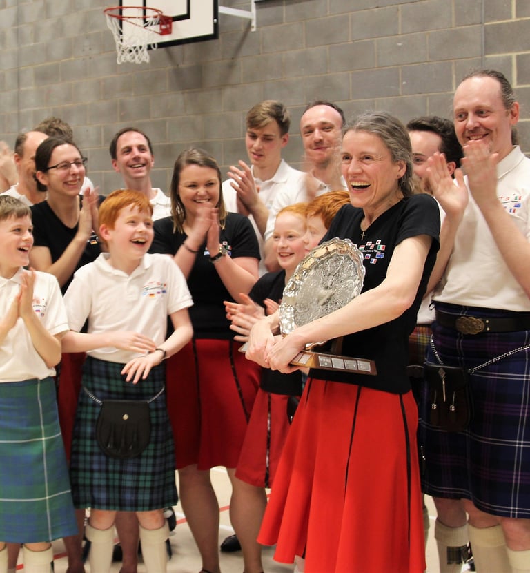 Laughing woman clutching a large trophy. Her team surrounds her, smiling and clapping.