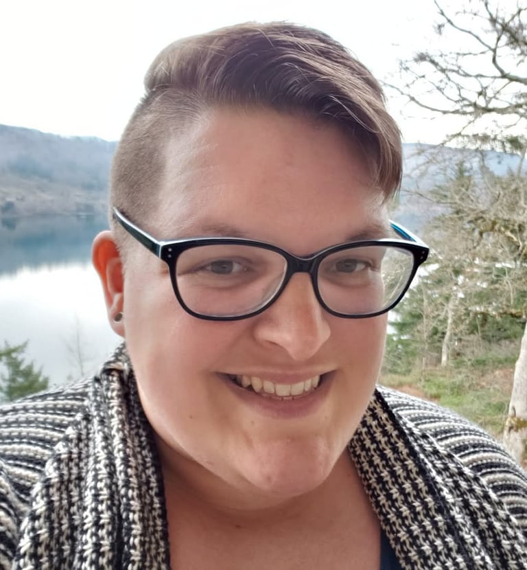 A person with glasses and short brown hair smiling with trees in the background