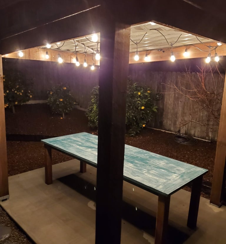 Reclaimed wood outdoor dining table under custom pergola with metal roof and lights. Colorado Springs remodeling.