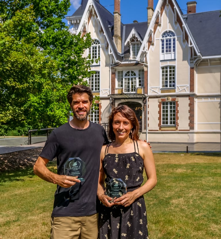 Un homme et une femme qui posent en souriant avec un trophée devant un chateau