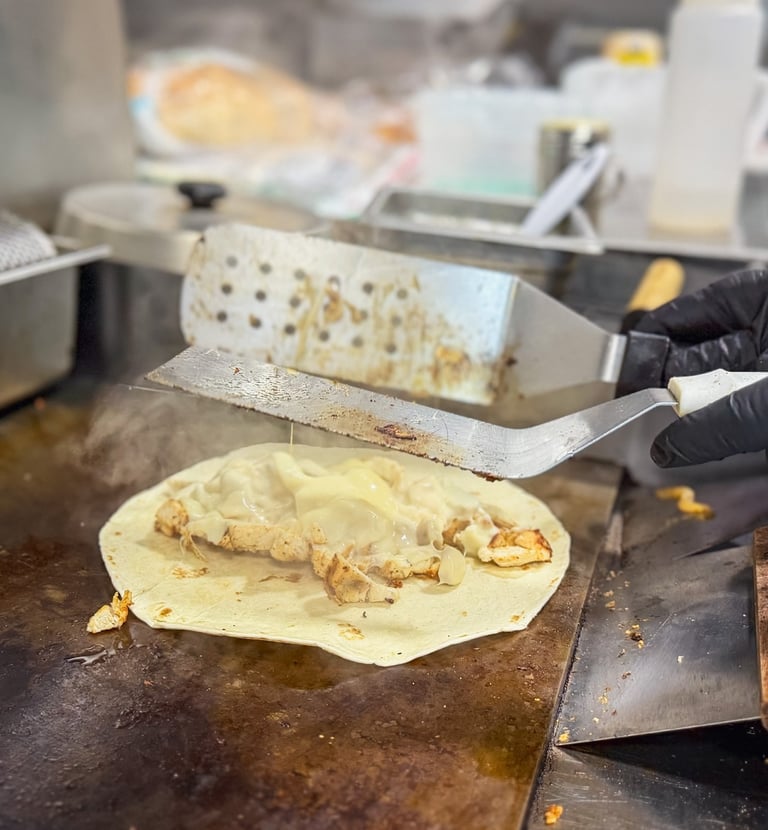 Chef grilling a chicken quesadilla with melted cheese on a flat top commercial griddle.