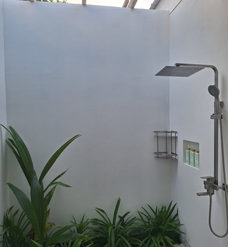 Modern outdoor rainfall shower with tropical green plants and white minimalist walls.