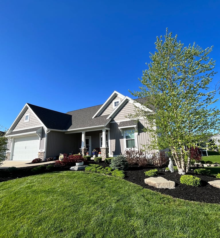 Modern single-family home with grey siding, professional landscaping, and green lawn under a clear blue sky.
