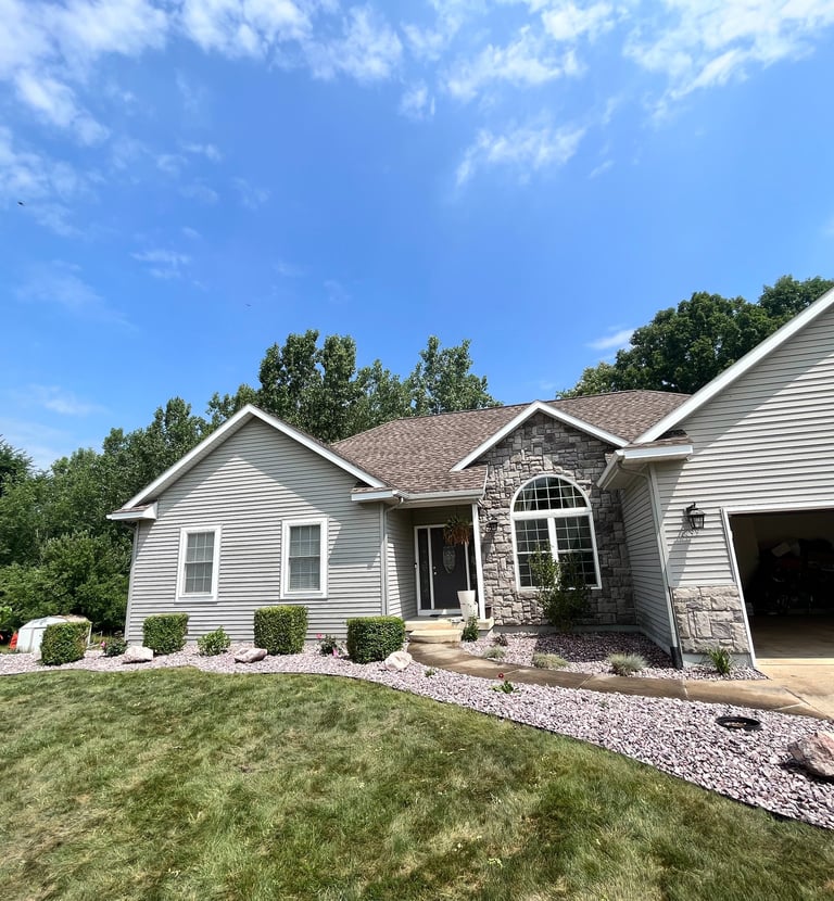 A single-family home with gray siding, stone accents, and manicured landscaping under a blue sky.