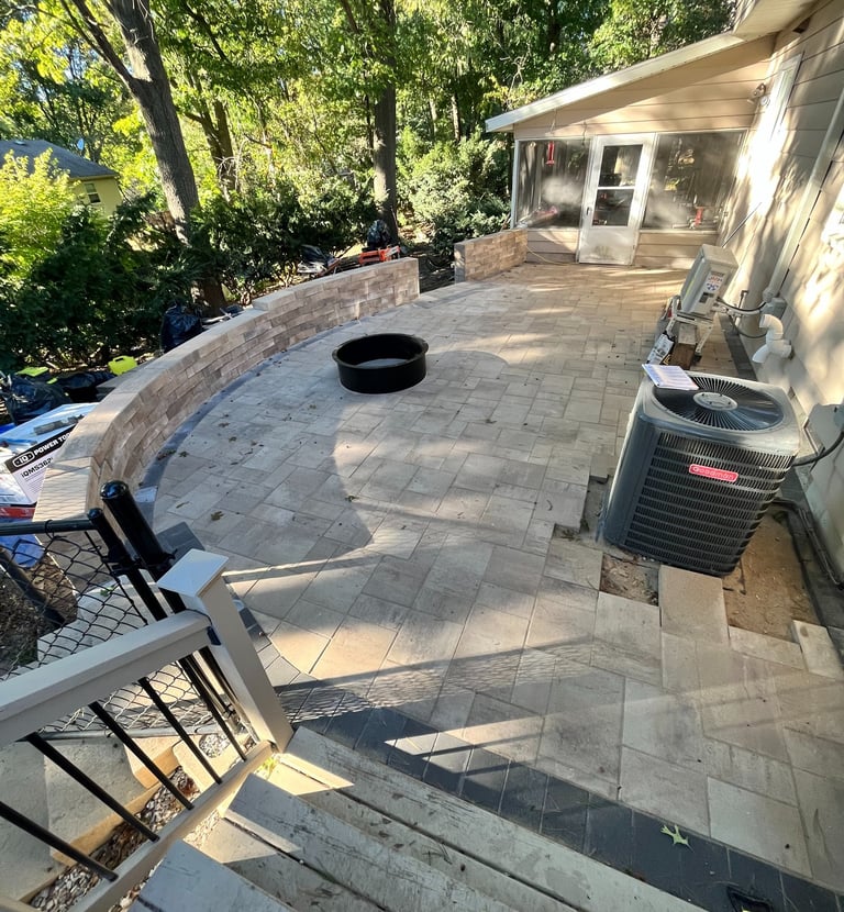 Custom paver patio installation with stone retaining wall and built-in fire pit area.