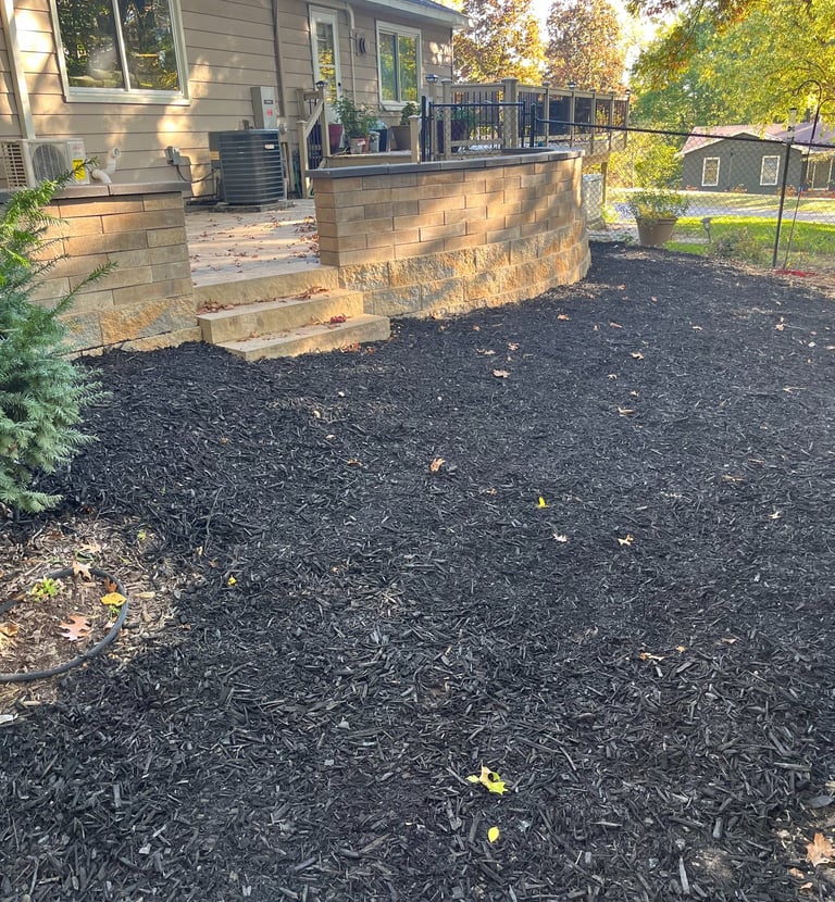 Backyard patio with stone retaining wall and fresh black mulch landscaping in a residential garden.