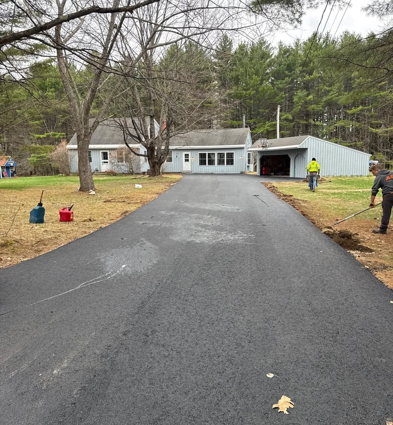 Professional asphalt driveway paving and smoothing for a residential home surrounded by trees.