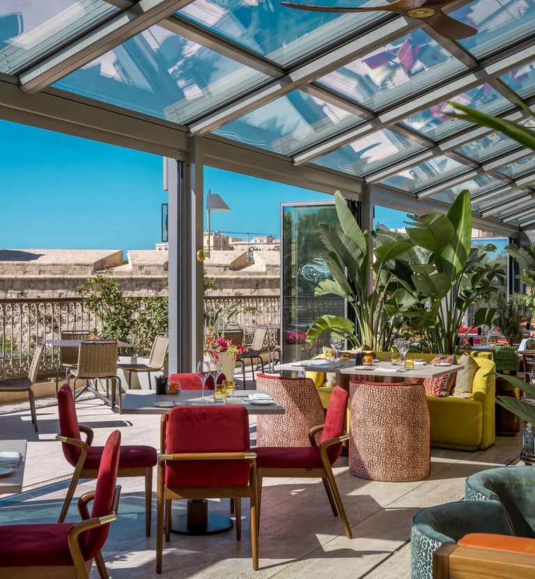 Luxury rooftop restaurant with a glass ceiling and views of a historic stone fortress under a clear blue sky.