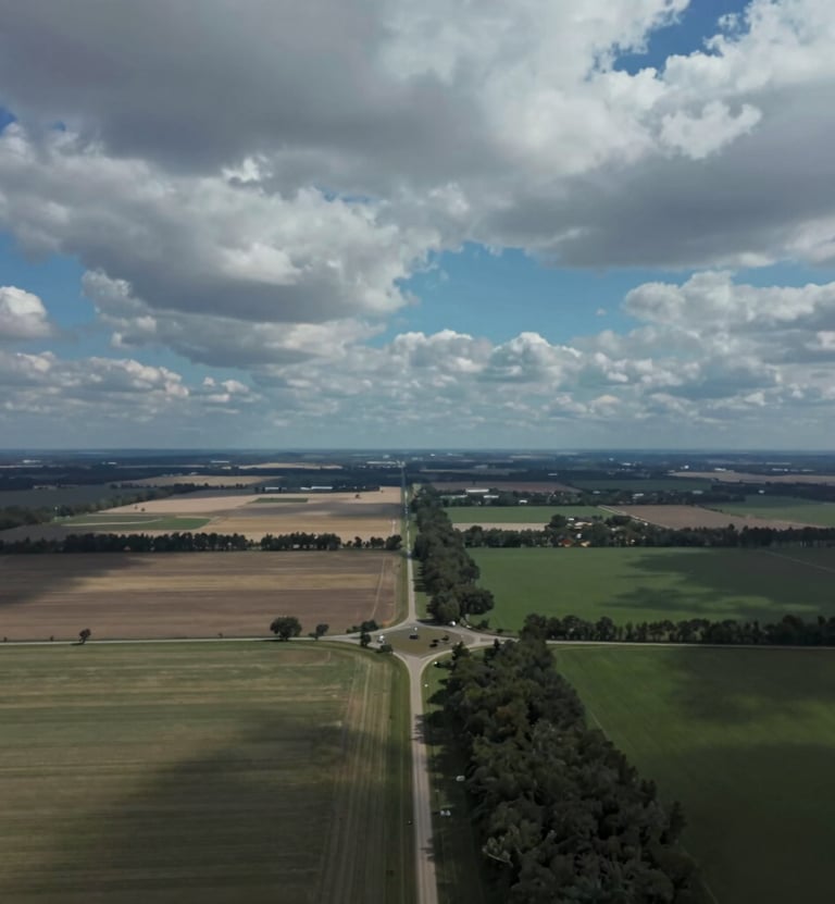 An aerial documentary-style photograph of a rural landscape under a dramatic sky, showing the intersection of nature and infrastructure. High contrast and professional grade, reflecting clear communication. Uses colors #263238 and #B0BEC5.