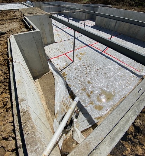 A concrete foundation for a new home construction featuring a plastic vapor barrier and steel support beams.