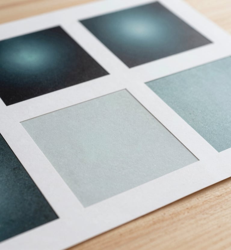 Fine art photography of printed research documents and design swatches laid out on a light wood surface. The lighting is soft and professional, highlighting the quality of the Pale Frost paper and Muted Teal ink.