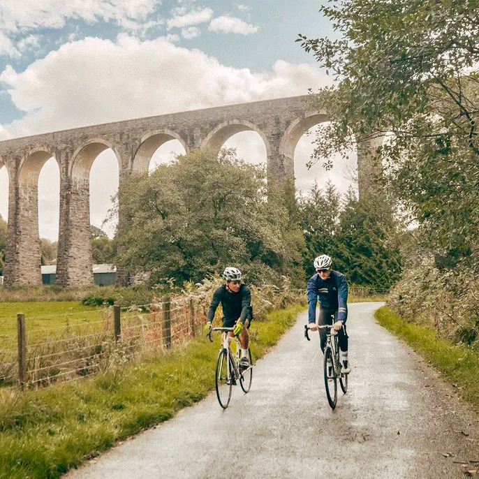 two people riding bikes down a path with a bridge in the background