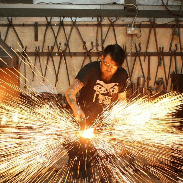A man is working on a piece of metal at a forge
