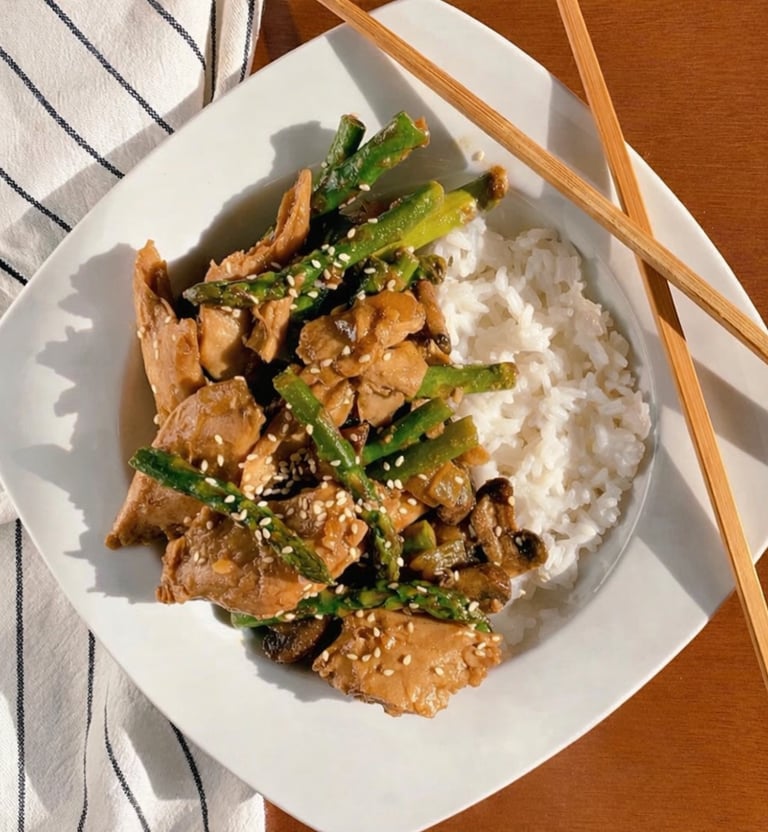 Not Chicken and asparagus stir fry with sesame seeds served over white rice with chopsticks.