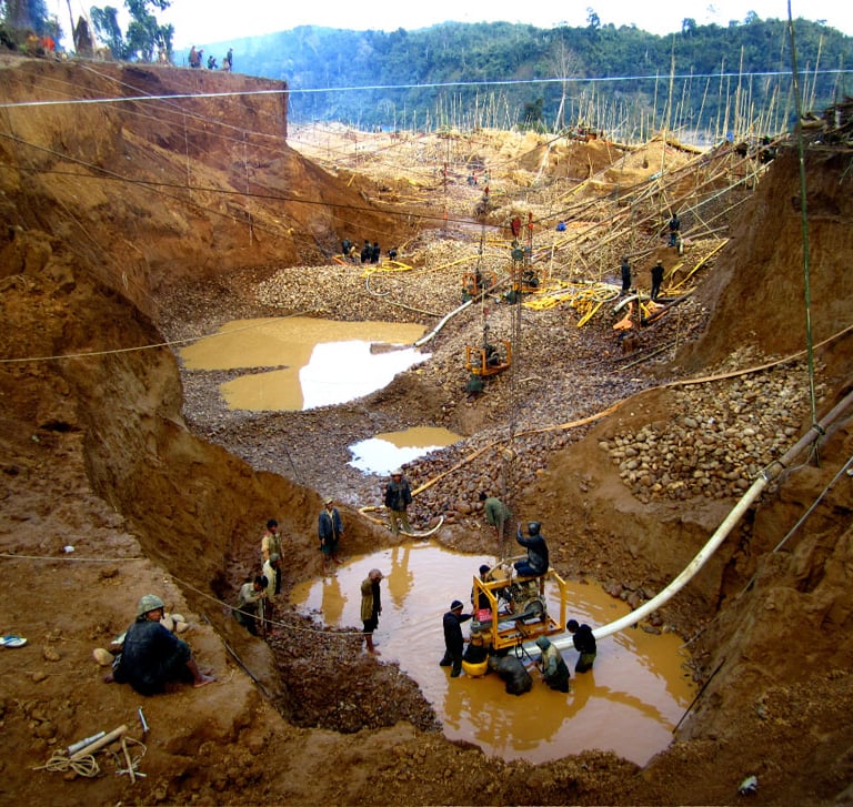 Miners working at an artisanal open-pit gold mine in a deep muddy excavation site with pumps.