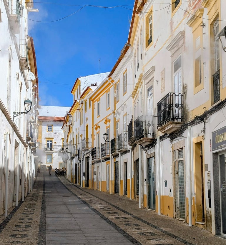 Narrow street in Elvas lined with whitewashed Alentejo buildings with yellow trim under a blue sky.