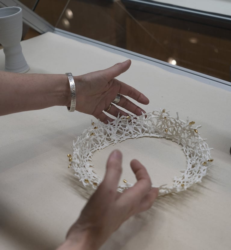 Two hands carefully place a white porcelain crown sculpture with gold details in a display case