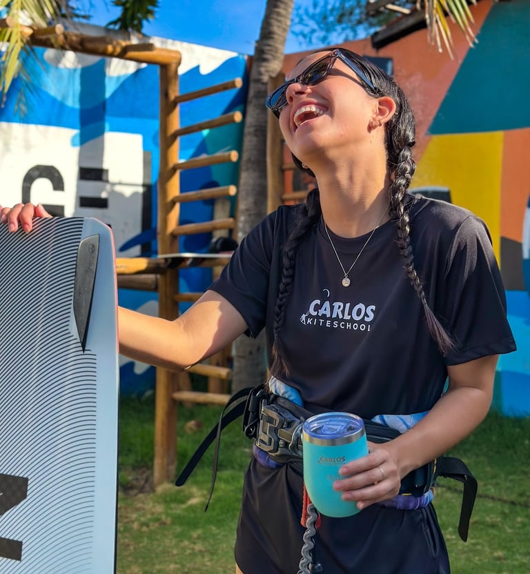 mulher jovem, sorrindo segurando um copo e uma prancha de kitesurf