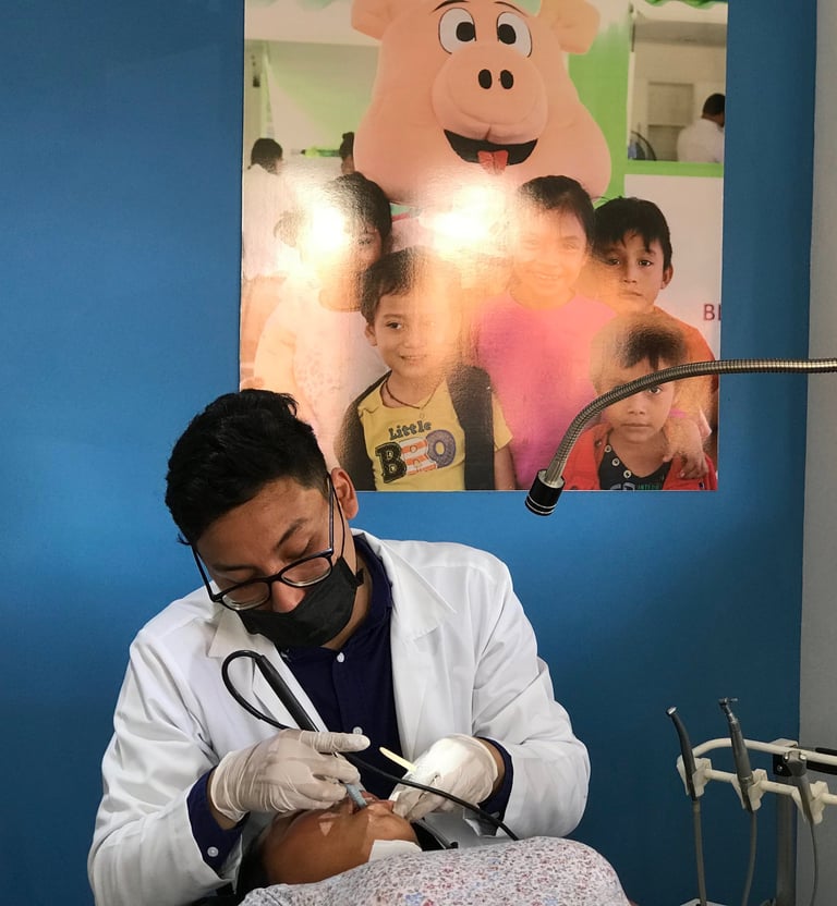 Odontólogo realizando un procedimiento dental a un paciente, con un póster infantil decorativo al fo