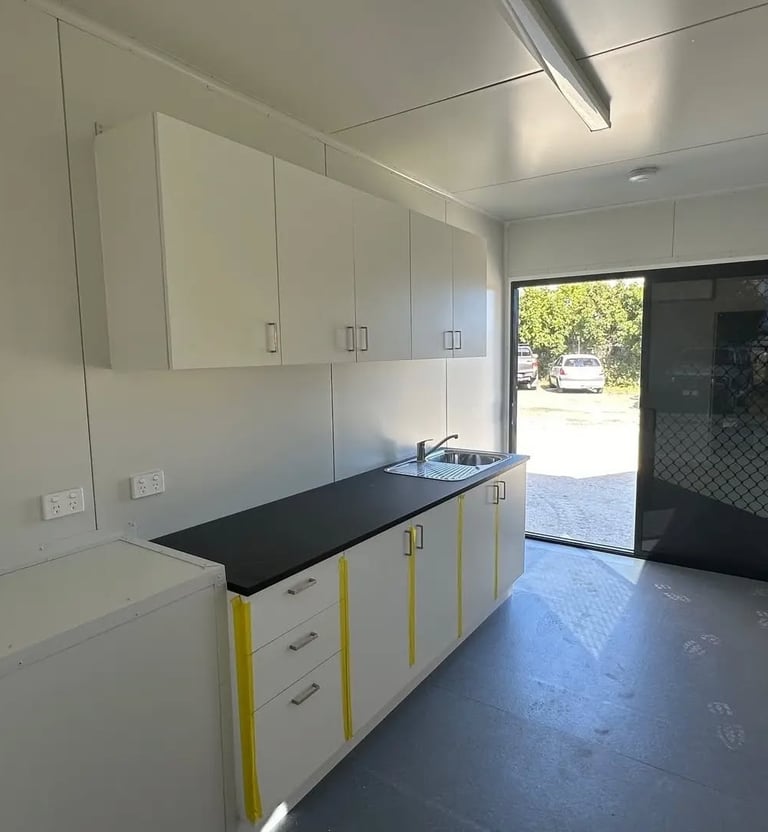 Modern portable cabin kitchenette with white cabinets, black countertop, and stainless steel sink.
