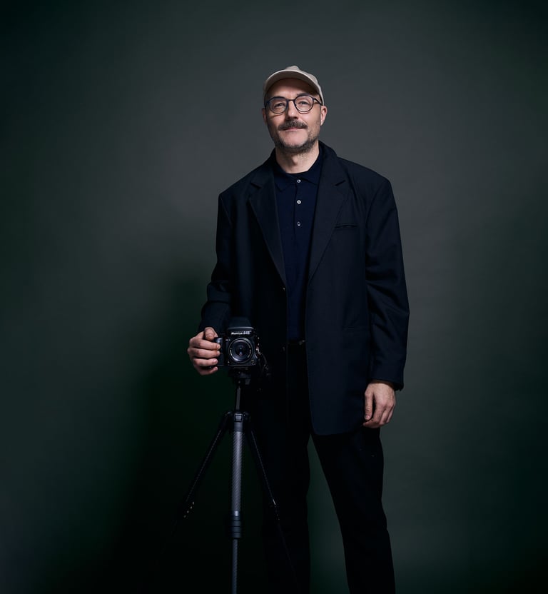 Professional photographer with mustache posing with a digital camera on a tripod in a studio.